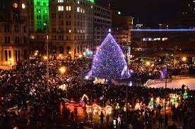 A lit christmas tree in the center with a crowd of people surrounding it. 