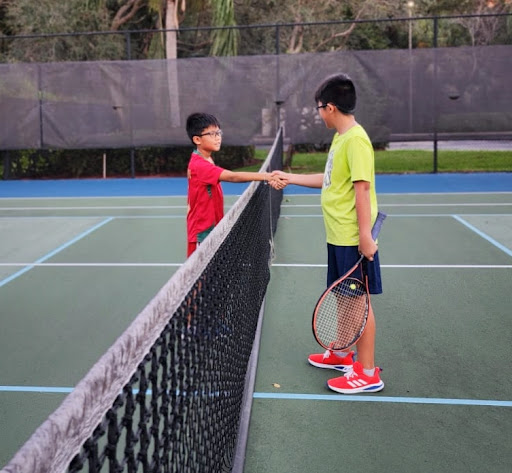 A picture of two tennis players shaking hand and showing sportsmanship after playing a match of tennis.