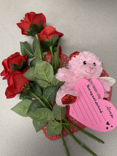 Red roses, pink teddy bear, and letter on a desk